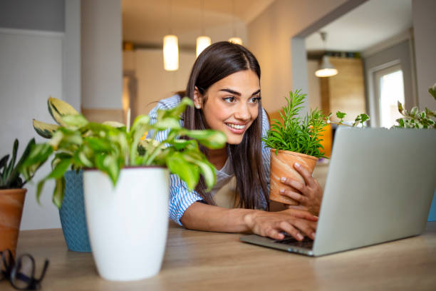 Woman happily shopping for plants online at home, surrounded by potted plants.